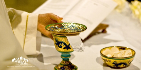 Priest touching a chalice and a bowl of wafers sitting on a table.